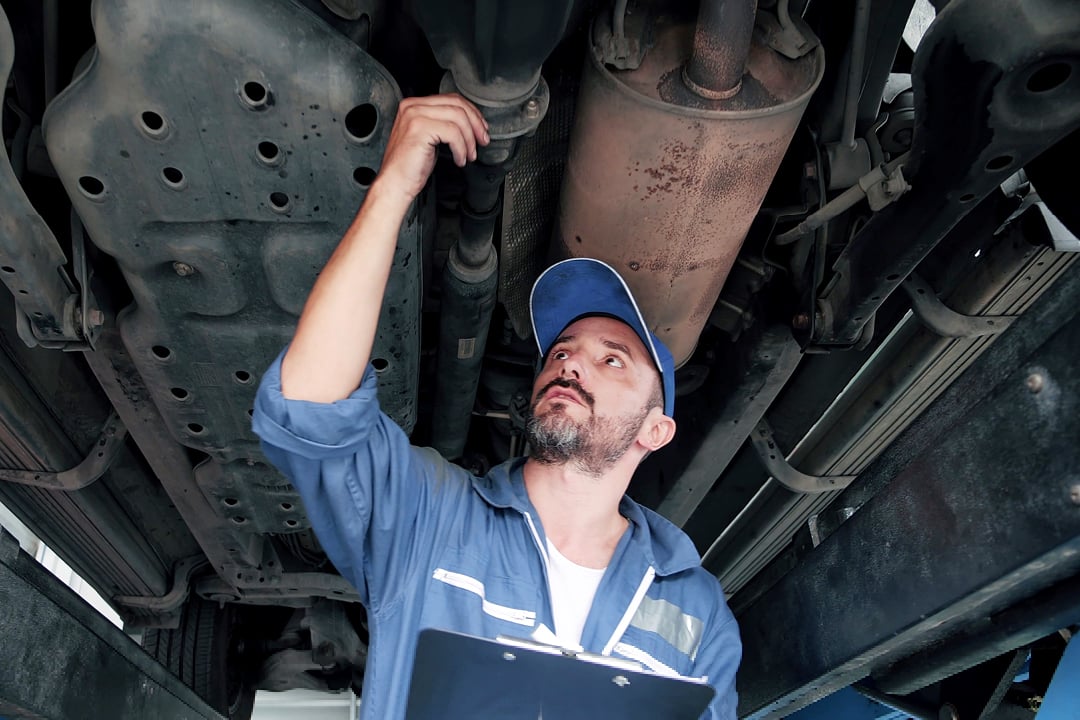 Mechanic with clipboard inspecting underside of car