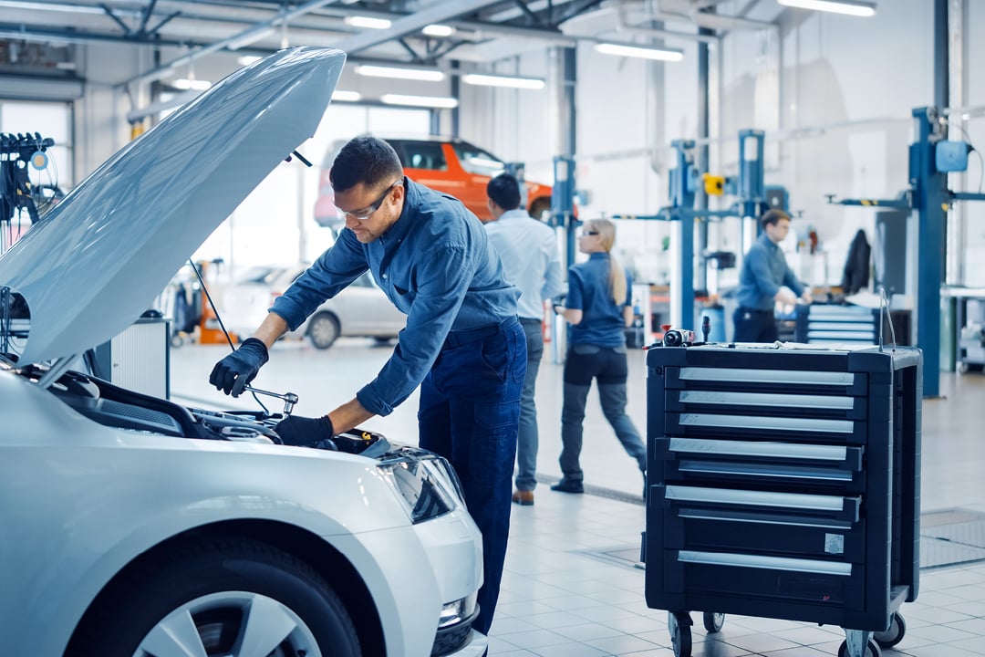 Mechanic in safety glasses repairing car in clean auto repair shop