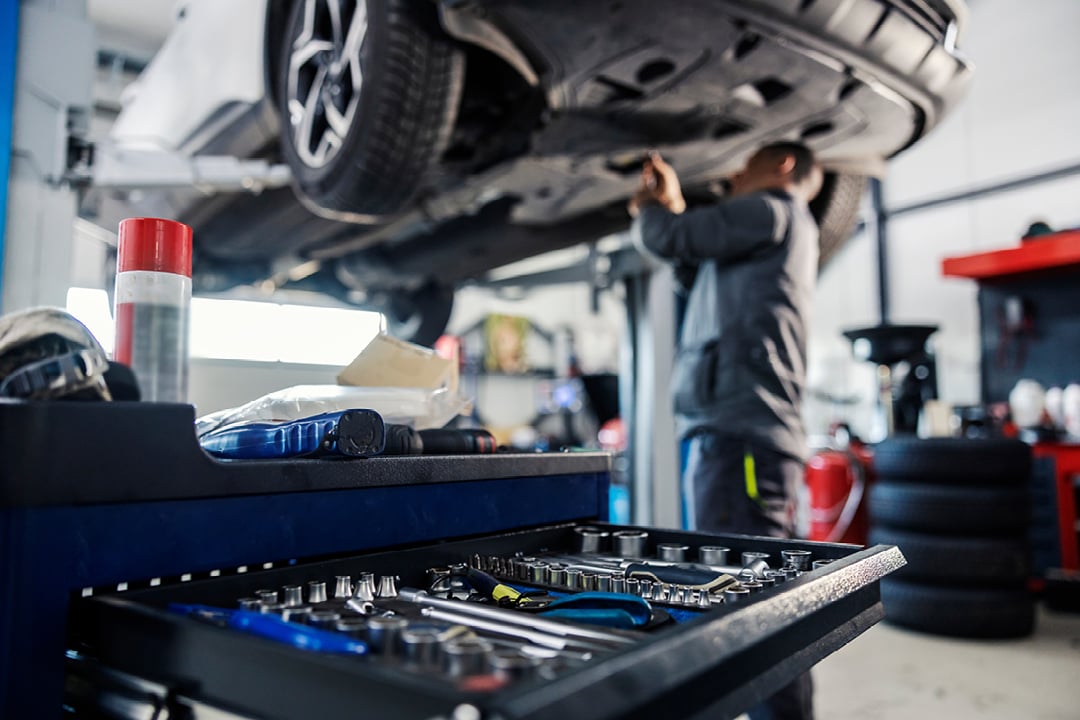 Toolbox tools in focus with mechanic repairing car in background