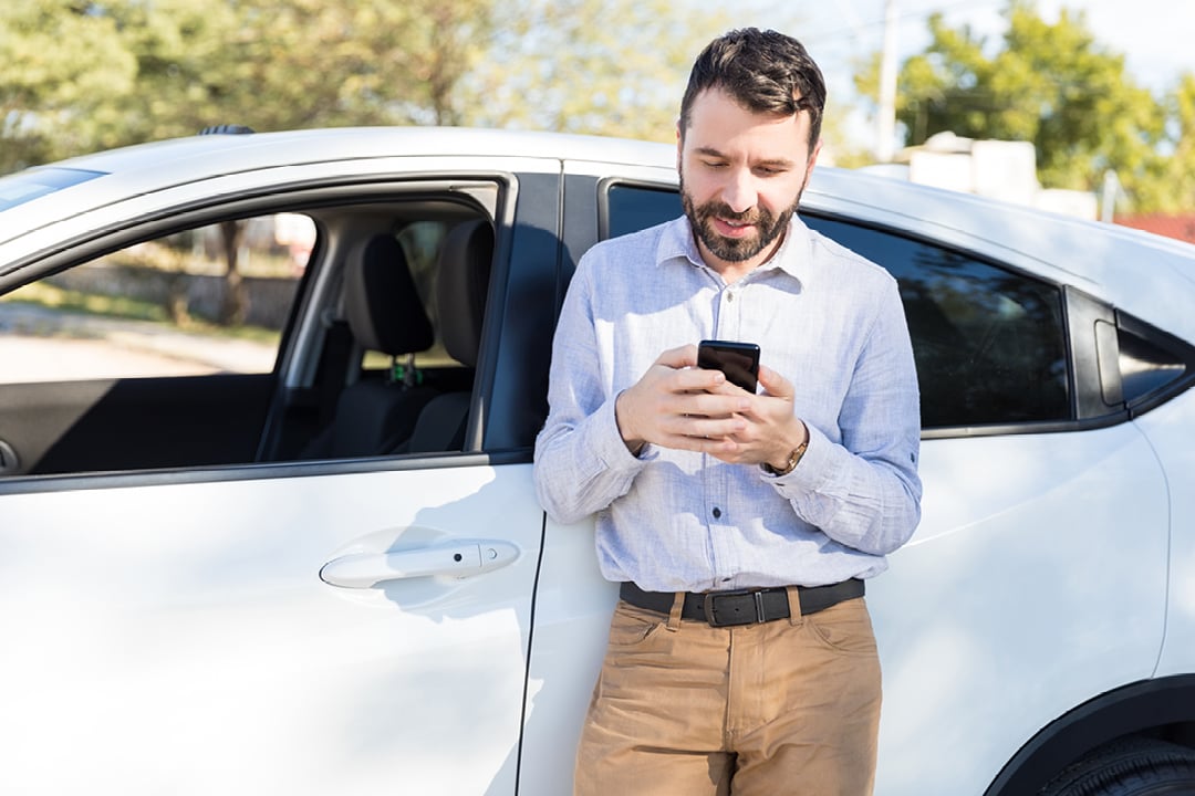 Car owner using a mobile phone beside a white car