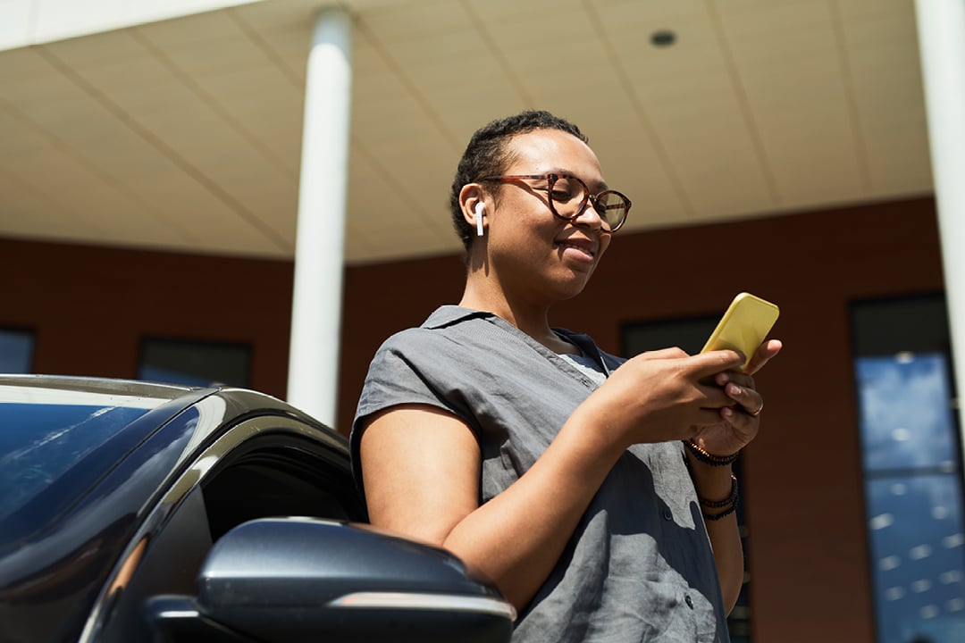 Woman exiting car while reading message on smartphone