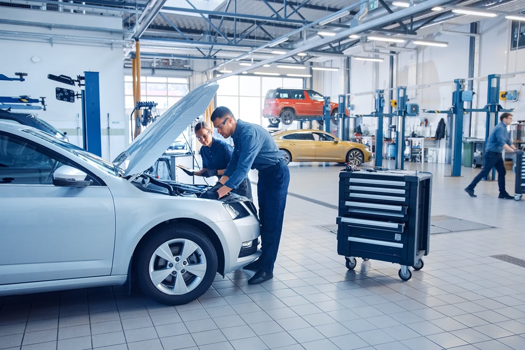 Mechanics inspecting a car while technician reviews diagnostics on a tablet